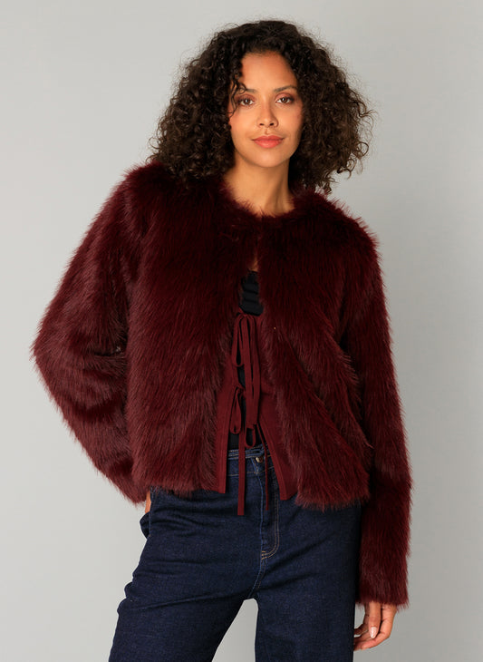 Woman wearing a wine coloured faux fur jacket against a grey background
