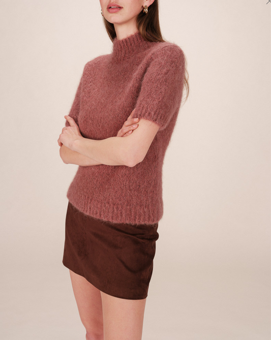 Person wearing a dusky rose, short sleeved sweater and brown skirt on a plain background