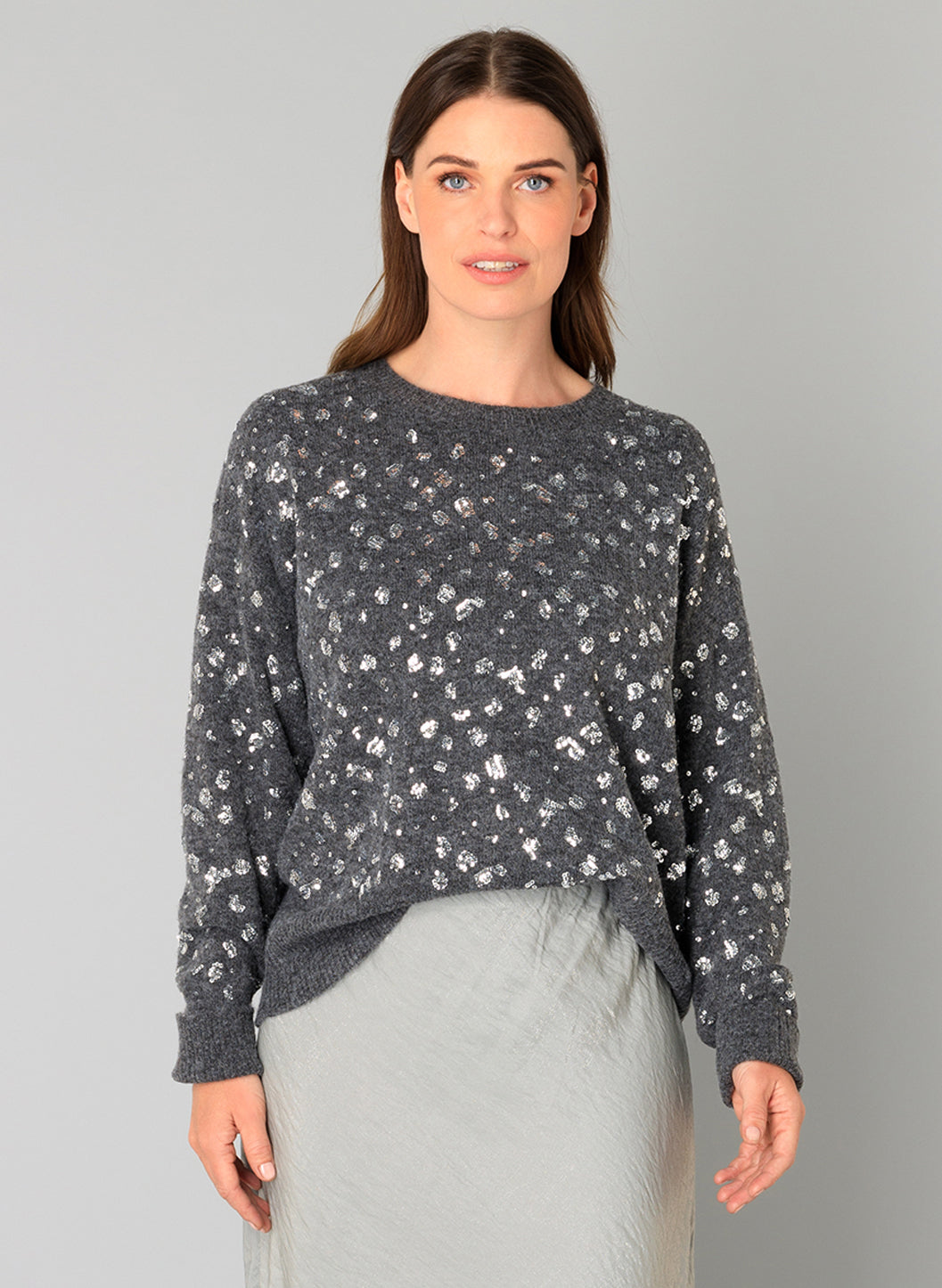 Woman wearing a grey sweater with a sparkle pattern on a plain background