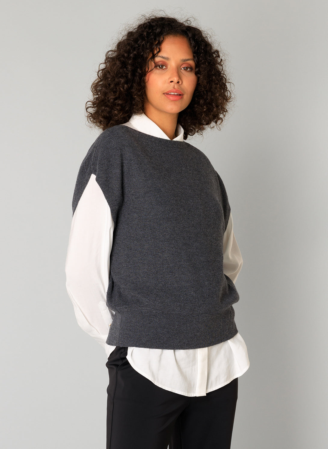 Woman wearing a dark grey sweater vest over a white shirt 
