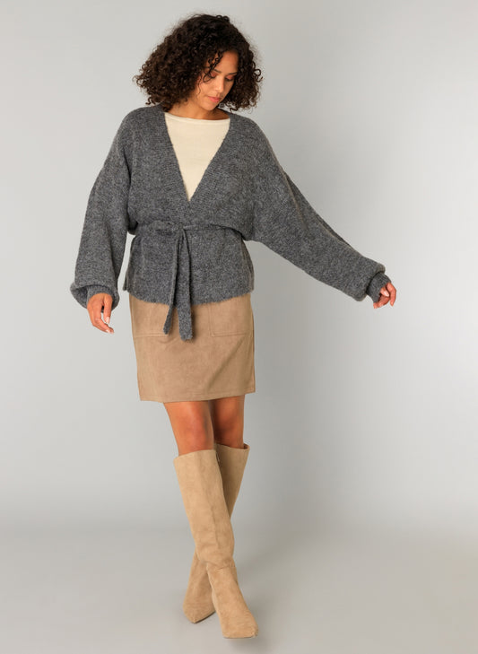 Woman wearing a gray cardigan with optional waist tie, beige skirt, and tan knee-high boots 