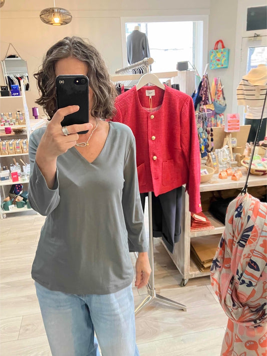 Person taking a mirror selfie wearing a gray soft v neck top and blue jeans in a store.