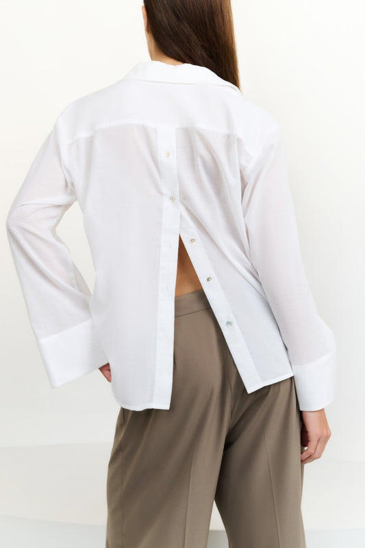 Person wearing a white open-back blouse and beige pants on a plain background