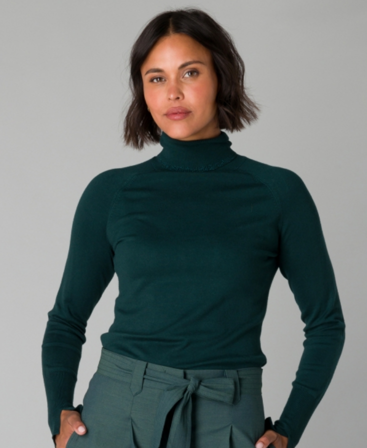 Woman wearing a dark green turtleneck sweater against a gray background