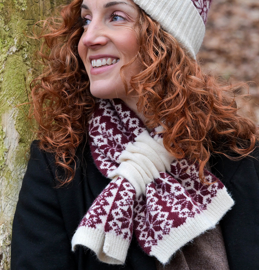 Woman wearing a white and wine coloured patterned scarf and hat, standing against a tree.