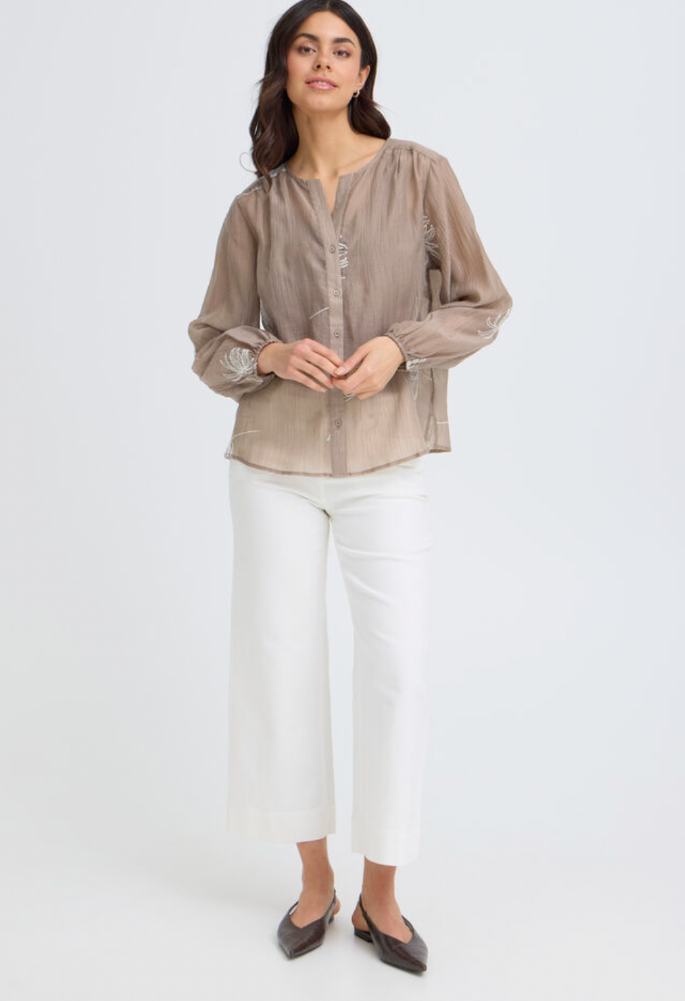 Woman wearing a beige blouse and white pants on a white background